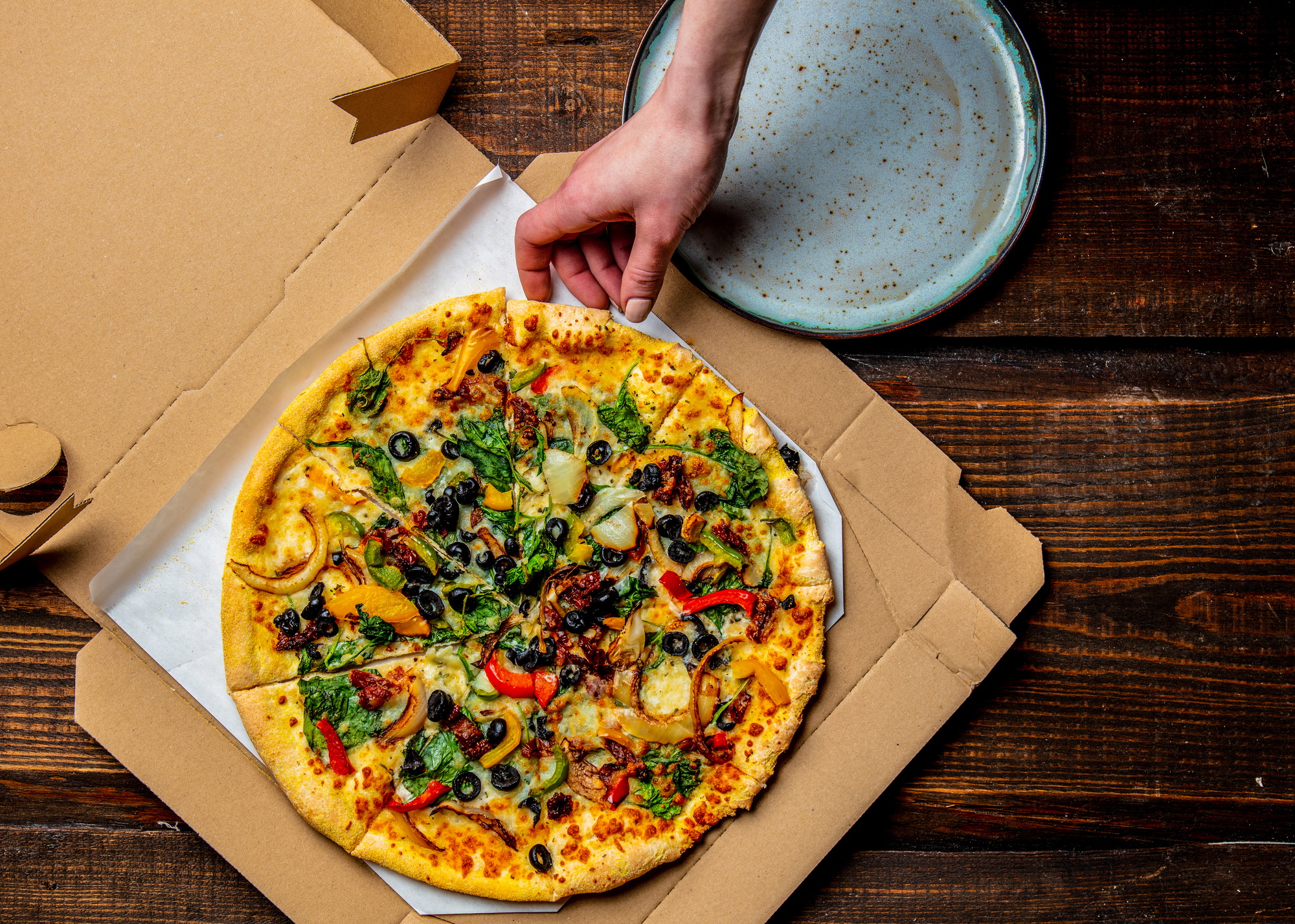 woman hand takes a mediterranean Pizza with olives and cheese from cardboard in a plate